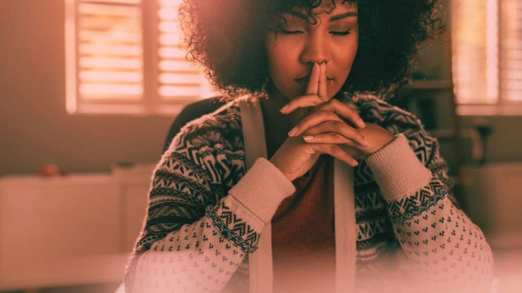 A woman sitting at a table with her pointer fingers to her lips engaging in mindfulness