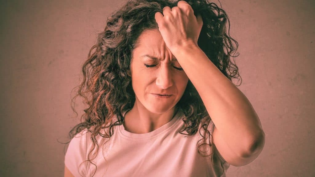 A stressed woman grips the front of her hairline in frustration. She is struggling with emotional sobriety.