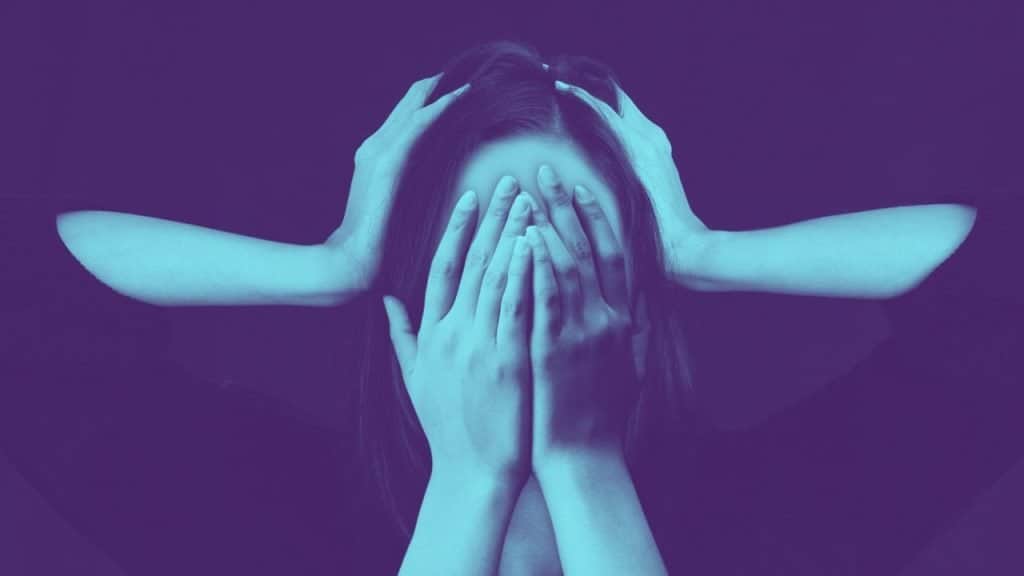 A person with hands over their face and ears wrestling with stress in sobriety