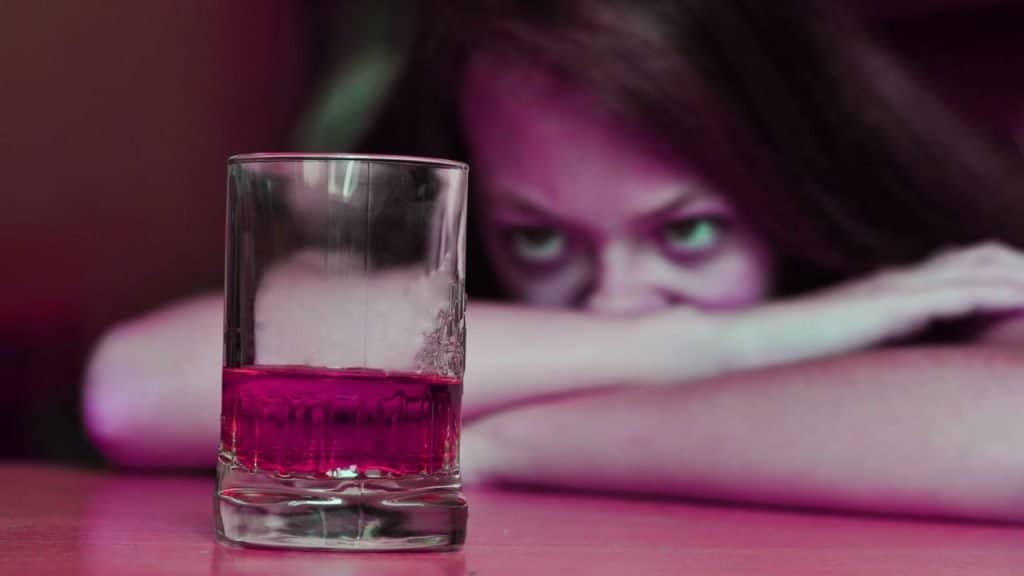 A woman stares at a glass of whiskey on the table contemplating relapse