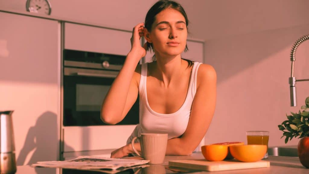 A happy, healthy woman closes her eyes and relaxes in her kitchen