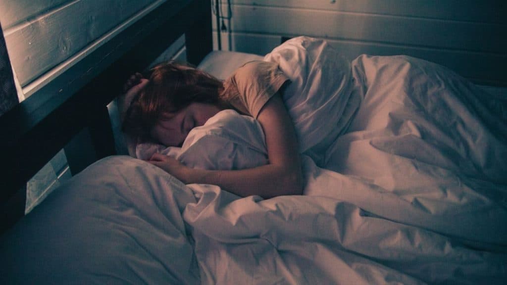 A woman with good sleep hygiene is asleep in a cozy bed with a white comforter and dark lighting
