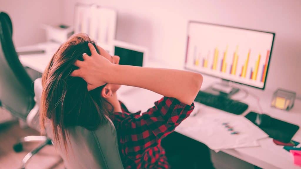 A woman sits back in her office chair, hands on her head. She is struggling to cope with stress.