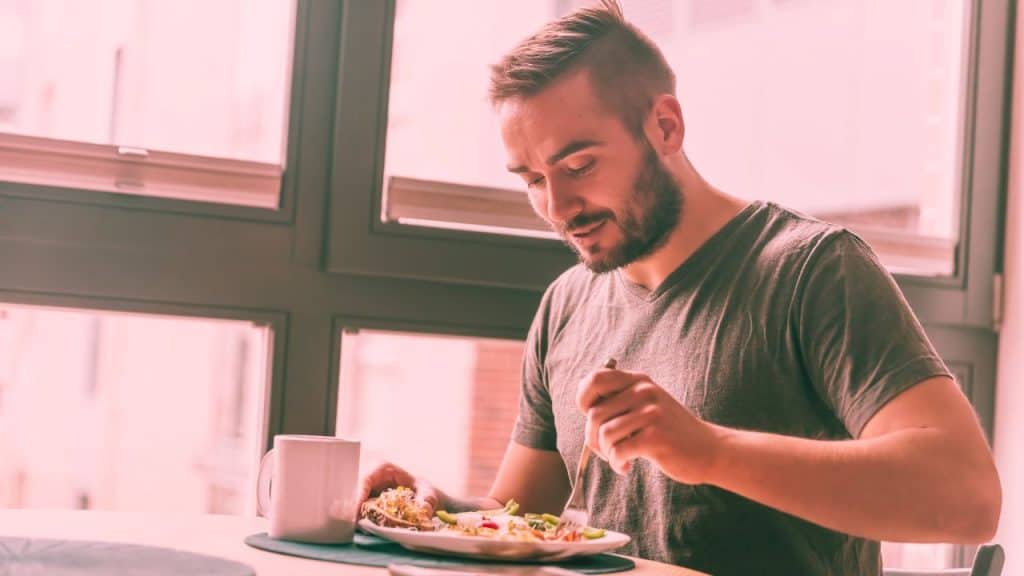 A man sits down at a table eating a healthy breakfast, smiling, stress-free