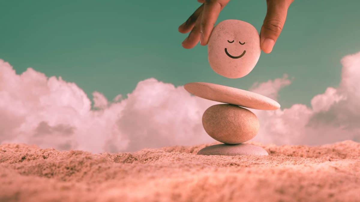 A hand placing a rock with a smiley face drawn on it atop three other stones