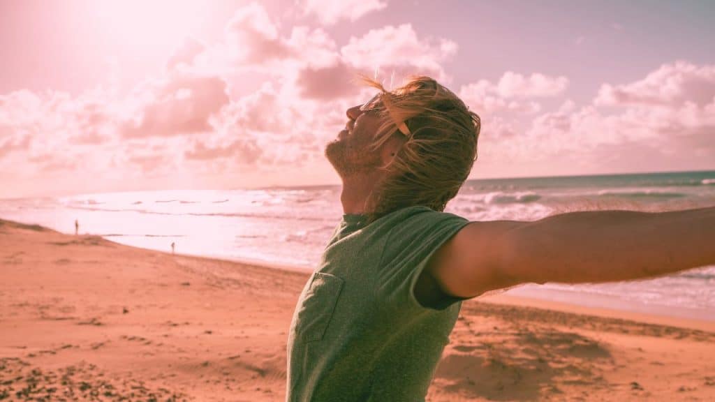 a sober man opens his arms in joy while on a beach