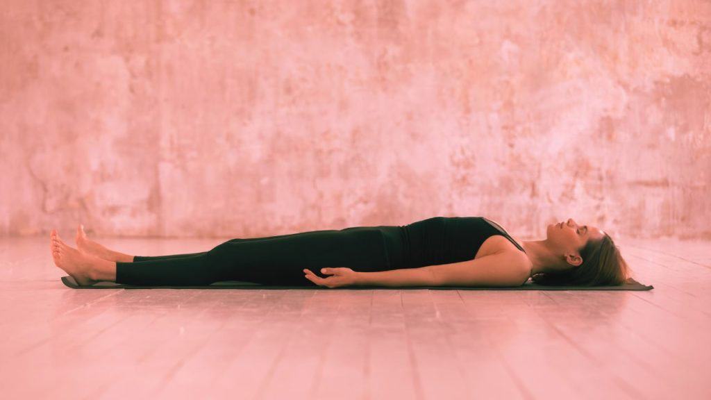 A woman lays on the ground doing a body scan meditation as part of her shadow work practice