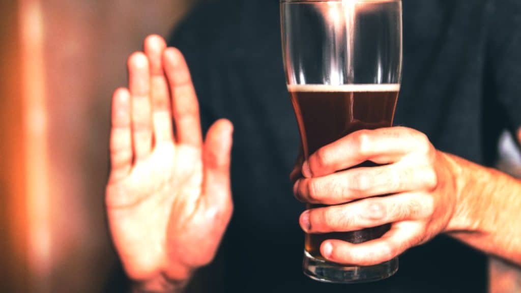 A man holds a large glass of beer in one hand and holds out his other in a stop gesture
