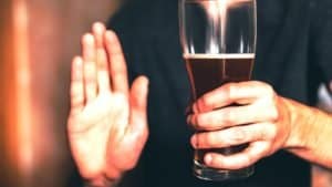 A man holds a large glass of beer in one hand and holds out his other in a stop gesture