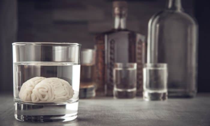 brain inside a glass of liquor with liquor bottles in the background