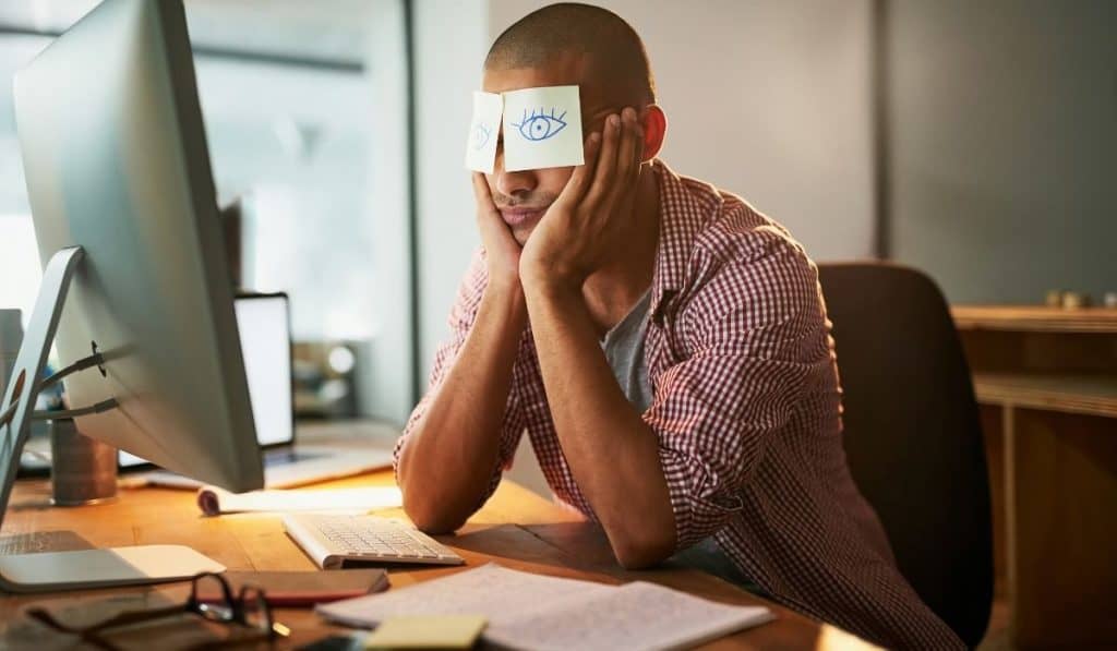 Man with elbows on desk pulling an all-nighter to fix his sleep schedule