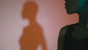 A profile of a woman in shadow while her shadow projects on the wall