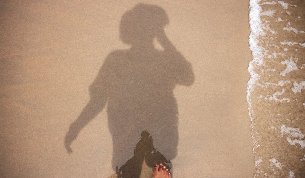 man photographing his shadow on the beach