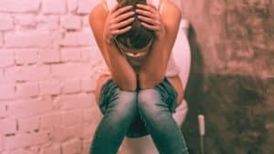 A constipated woman sits on the toilet in visible pain