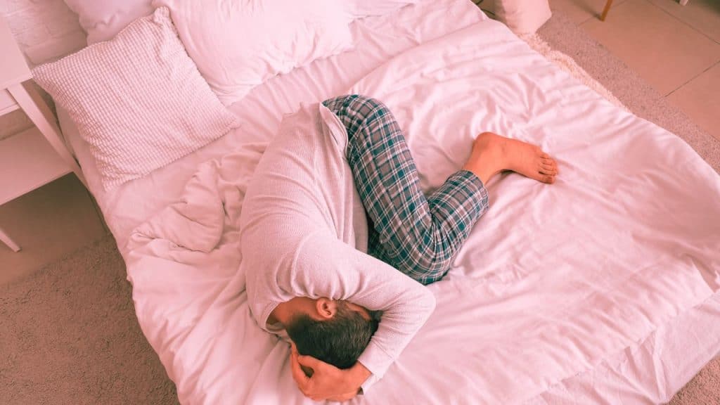 A man huddles together on his bed suffering from an alcohol-induced panic attack