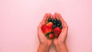 Two hands hold strawberries and blueberries