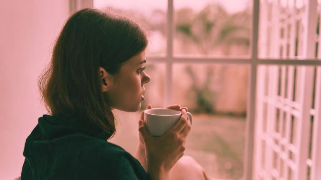 A woman who's been love bombed then ghosted looks out the window holding a cup of tea