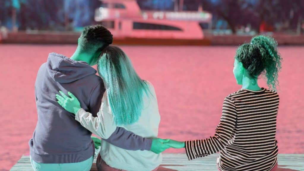 A man sits on a bench with his arms around his partner while extending his hand to another woman, signifying BPD monkey branching