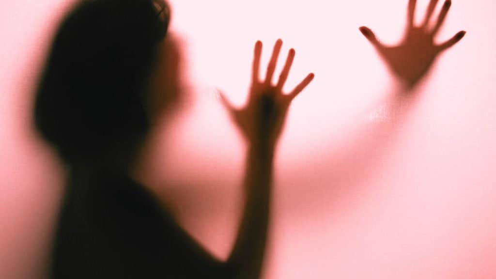 A shadow of a woman with hands up against a fogged glass pleading