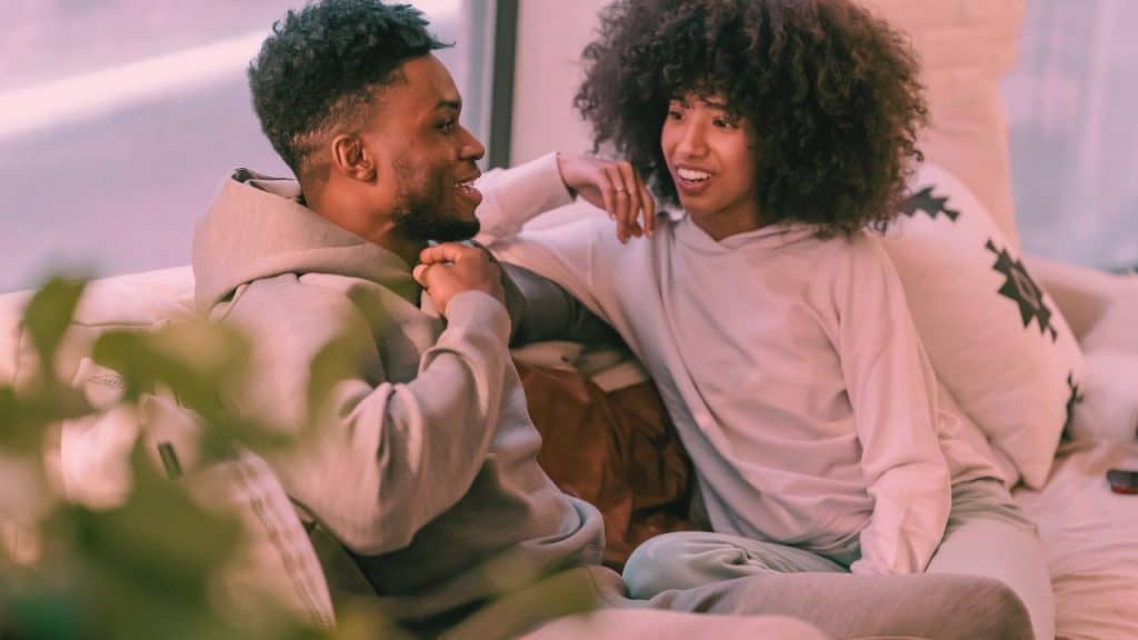 A man and woman sit on a couch talking with each other and smiling