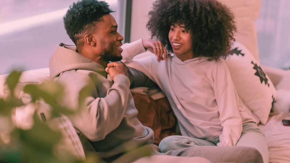 A man and woman sit on a couch talking with each other and smiling