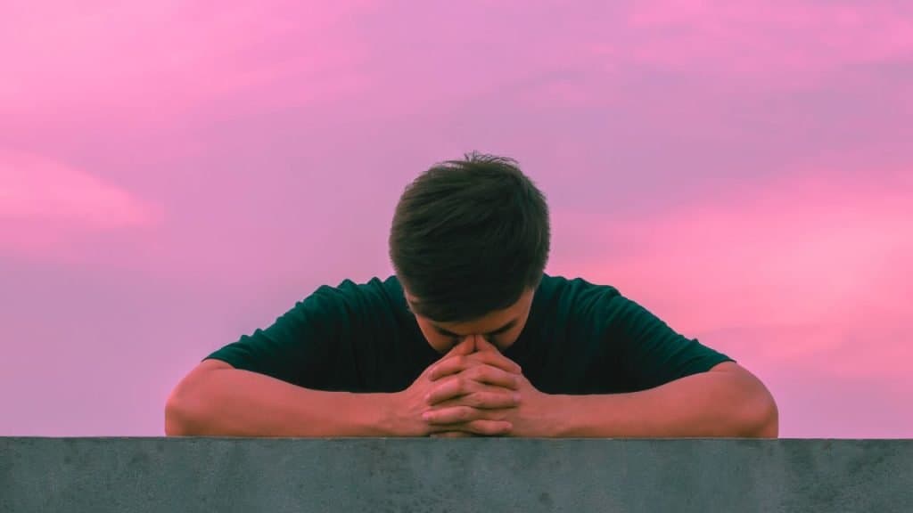 A man leans his arms on a ledge and puts his head in his hands prayer style