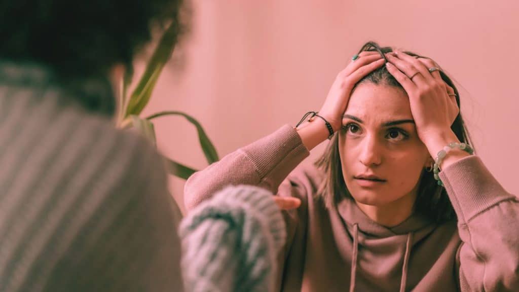 anxious avoidant woman sits with hands on head while partner points at her