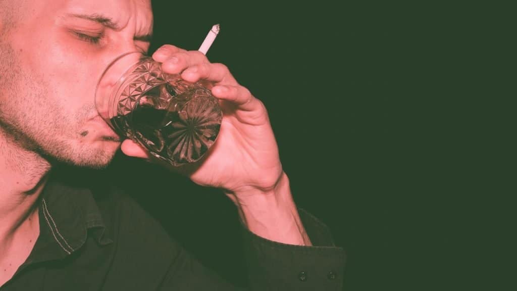 A man with BPD holds a cigarette and glass of whiskey, drinking