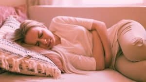 A woman lays down on the couch clutching her stomach in pain from aclohol