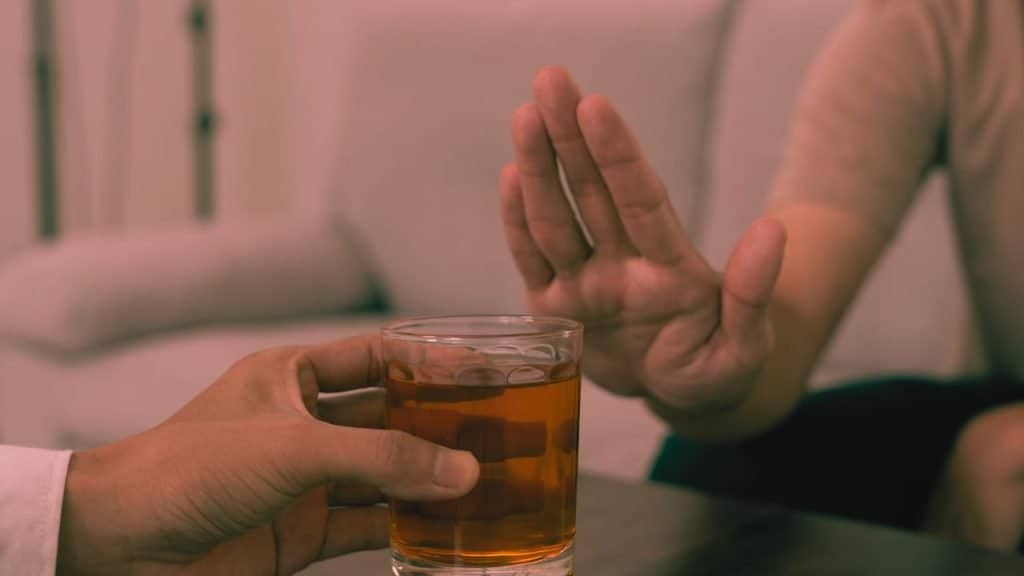 A hand rejects a glass of alcohol