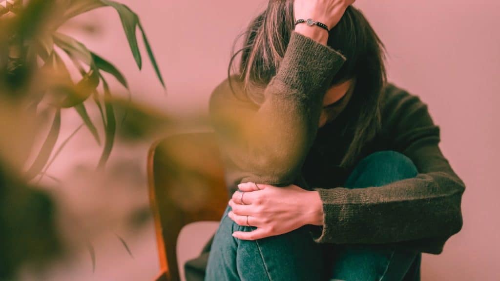 A woman with anxiety sits on the ground, wrapped up in her own arms, stressed