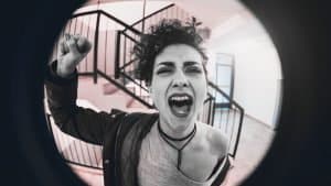 An angry drunk woman pounds on the door. We see her through the keyhole