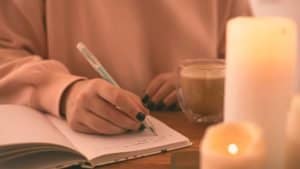 A woman sits at a table with her journal responding to shadow work prompts for relationships. There are three lit candles.