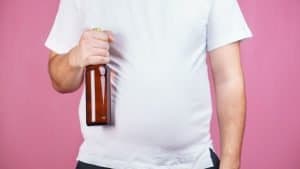 A man with a beer belly holds a bottle of beer