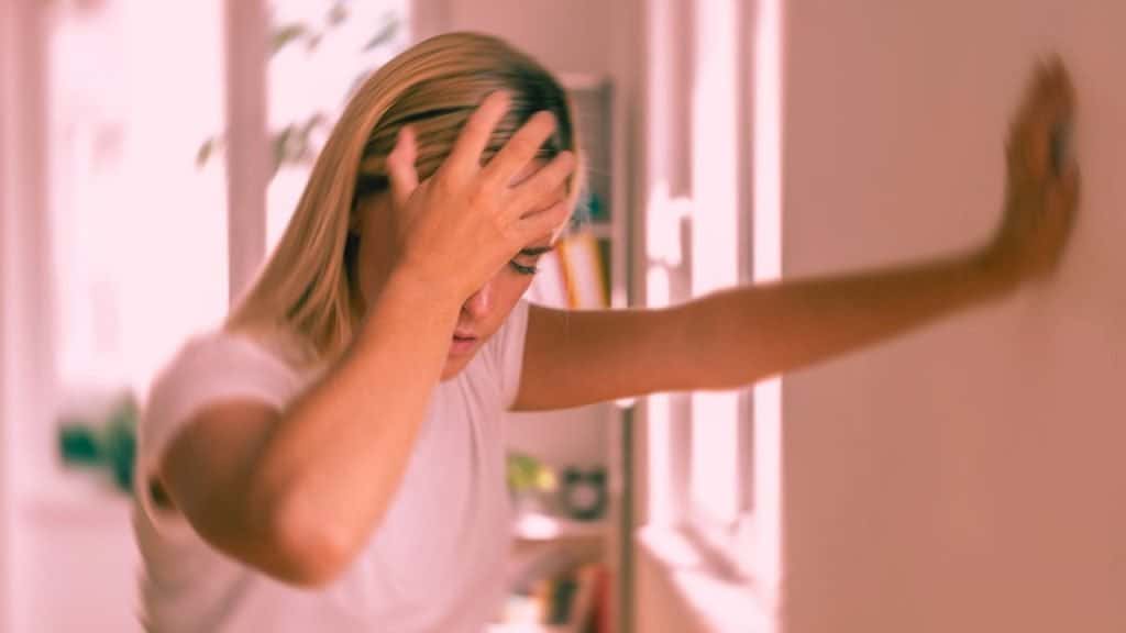 A woman leans against the wall, suffering from hangover shakes, hand on her head