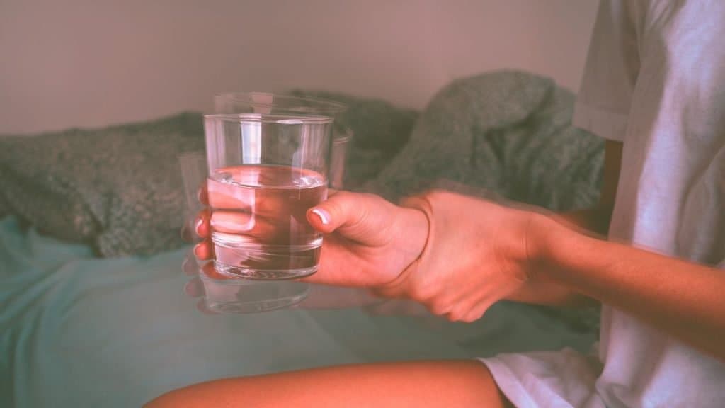 A woman shaking after drinking and trying to hold a glass of water