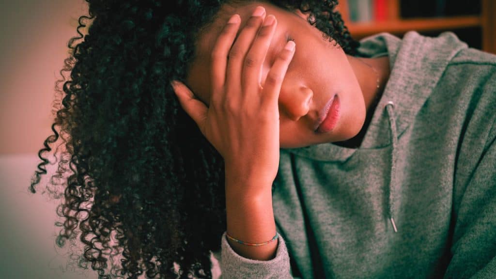A woman is stressed with anxiety and puts her hand over her eyes, tilting her head to the side