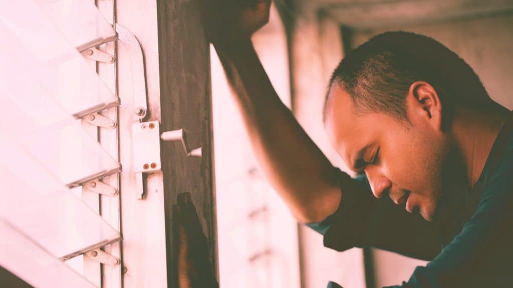 A man struggling with emotional reasoning leans against a window appearing stressed