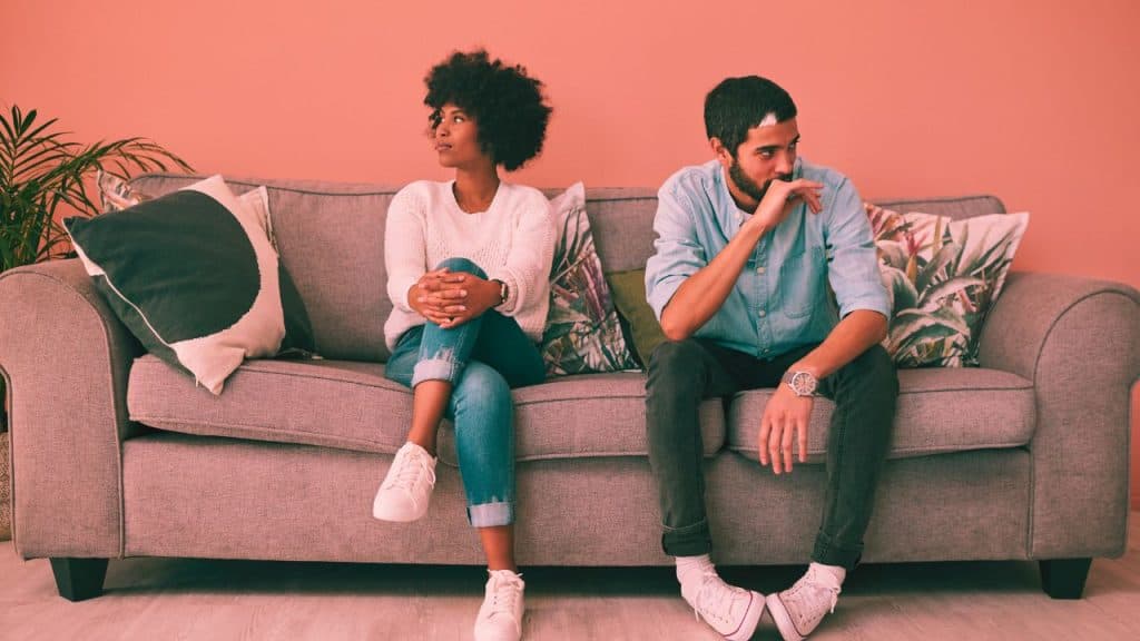 A couple sits on the couch looking away from each other