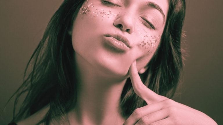 Close up image of a covert narcissist woman with her eyes closed puckering her lips and pointing to her face