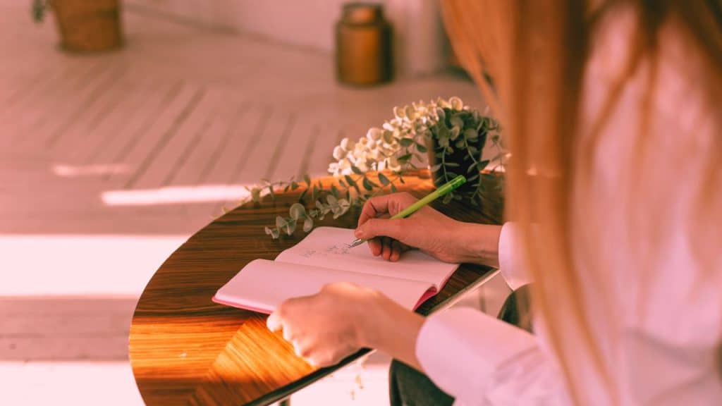 A woman writes her addiction recovery plan into a journal on a table